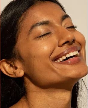 A woman smiling with her eyes closed in bright daylight